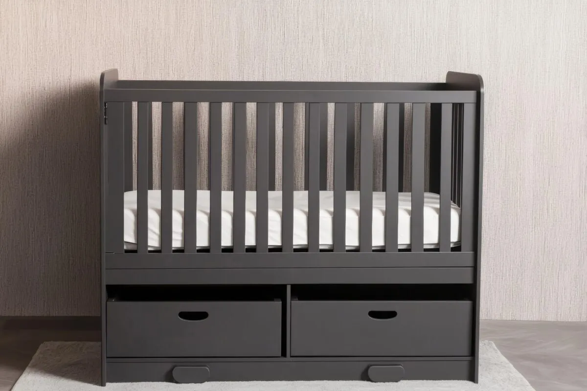 Berço evolutivo cinza com grades de madeira, colchão branco e duas gavetas de armazenamento na base, em quarto de bebê