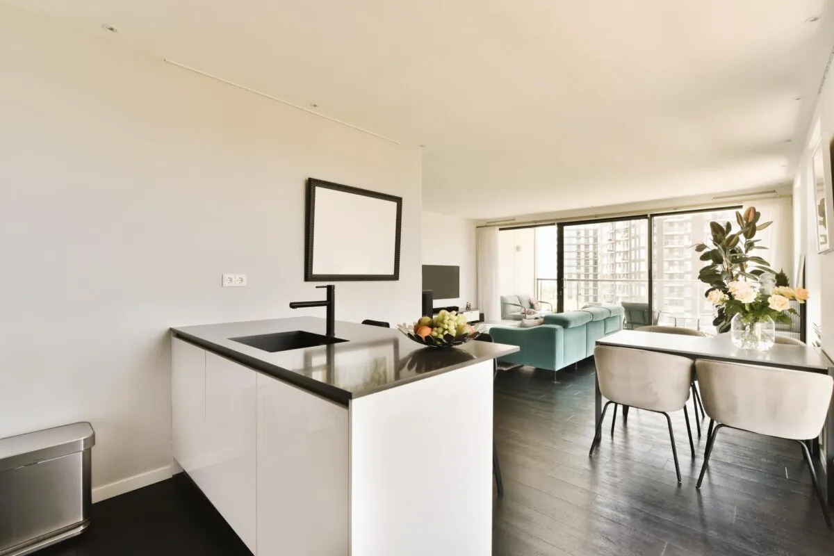 Cozinha americana com balcão branco e bancada preta integrada a uma sala com sofá e mesa de jantar