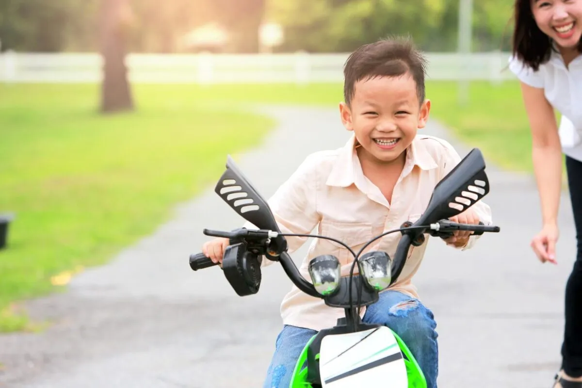 Menino sorridente pilotando uma moto elétrica em um parque